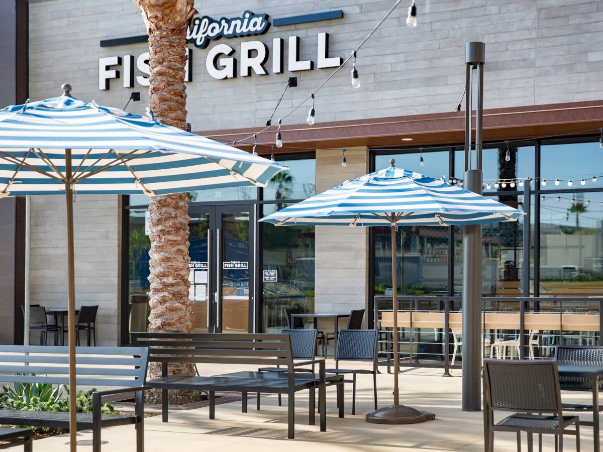 An outdoor dining area with striped umbrellas and seating in front of a restaurant named California Fish Grill.