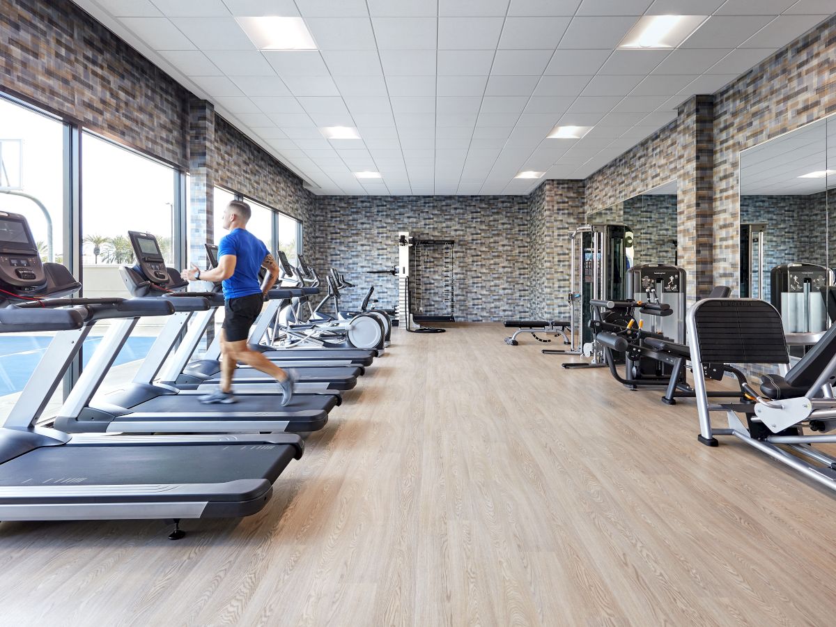 A person is running on a treadmill in a modern gym with various exercise equipment and large mirrors on the walls.