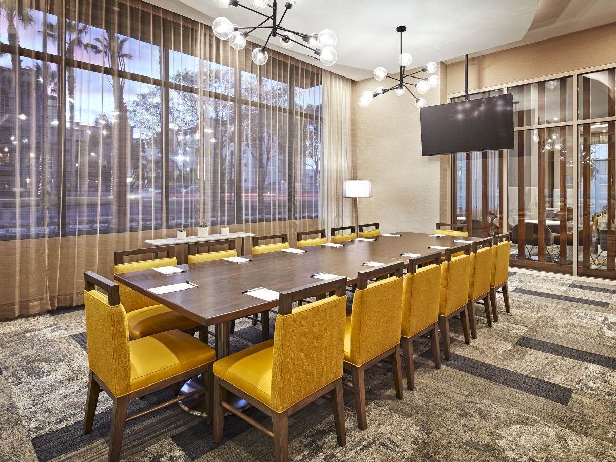 A stylish conference room with a modern design featuring a long table surrounded by yellow chairs and a large window.