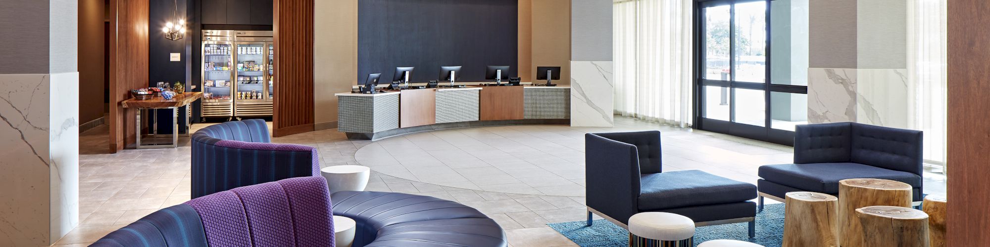 This image shows a modern lobby area with curved seating, various chairs and tables, a reception desk, and overhead lighting fixtures.