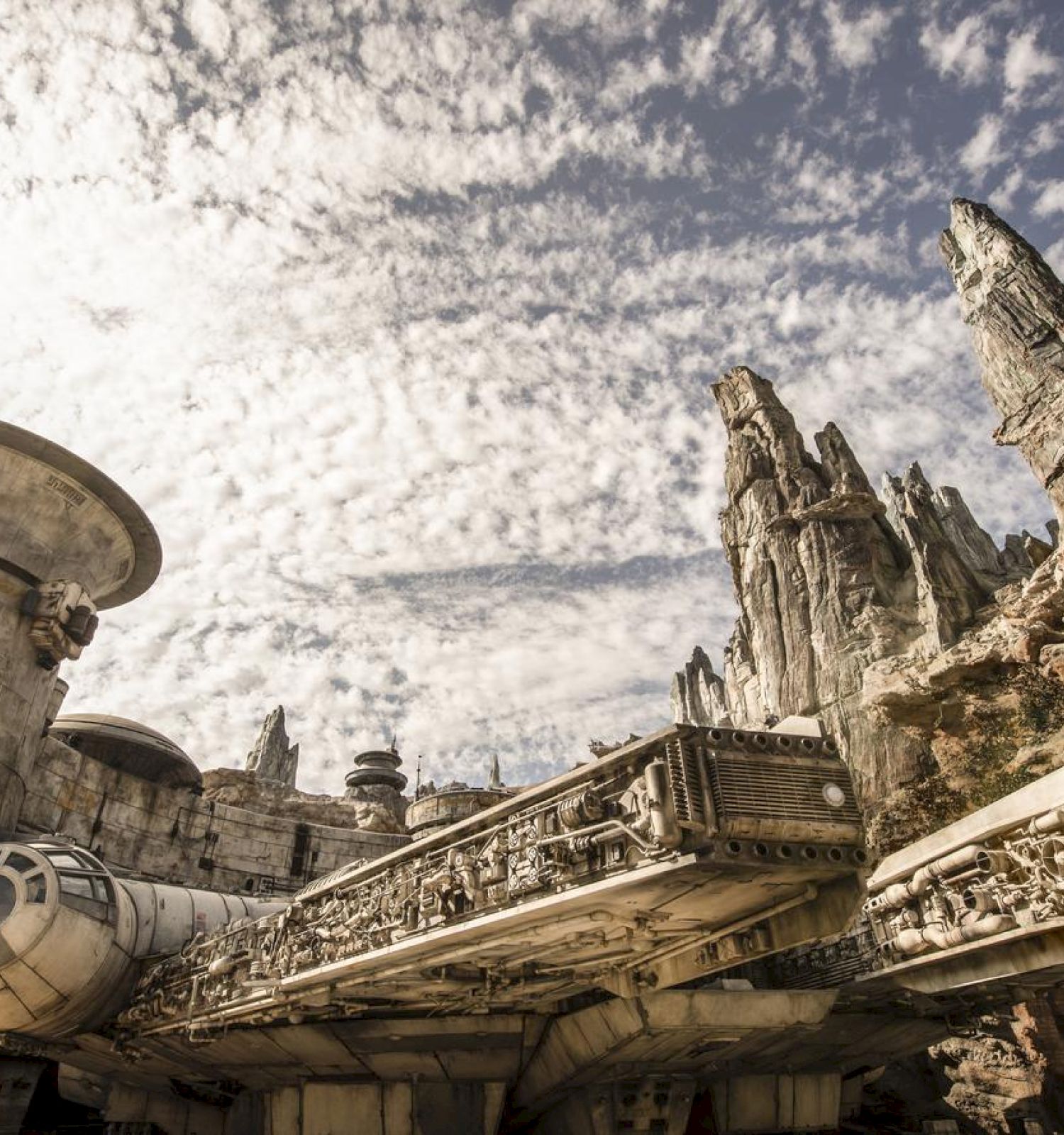 A large spaceship is docked amidst jagged rock formations under a partly cloudy sky, evoking a scene from a sci-fi universe.