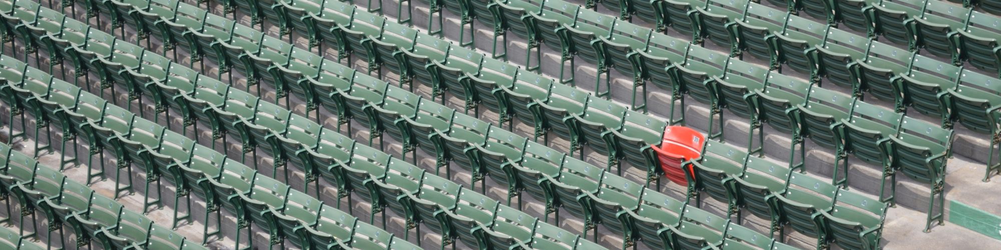 The image shows rows of green stadium seats, with one red seat standing out in the middle.