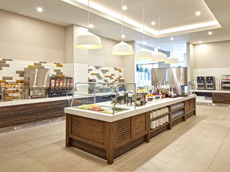 A modern self-service buffet with overhead lights, beverage dispensers, a variety of food items displayed, and a clean, contemporary design, ending the sentence.