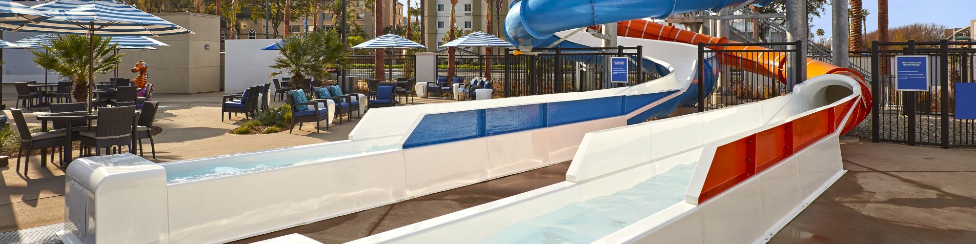 An outdoor water park with multiple colorful water slides, lounge chairs, palm trees, and a clear blue sky in the background.