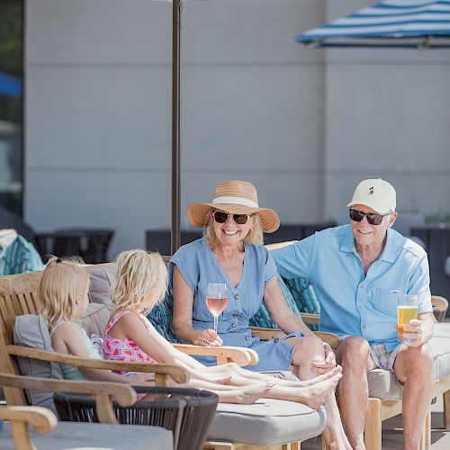 A group of people sitting outdoors under umbrellas, enjoying drinks and each other's company, with two children and two adults present.