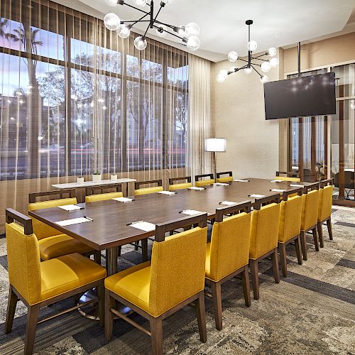 The image shows a modern conference room with a large table, yellow chairs, a TV on the wall, and stylish lighting fixtures, ending the sentence.