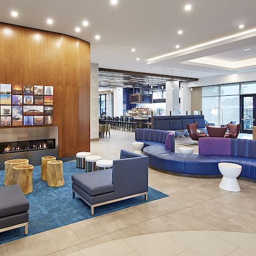 A modern lobby with seating areas, a fireplace, decorative wooden stools, and contemporary furniture against a backdrop of warm wooden panels.