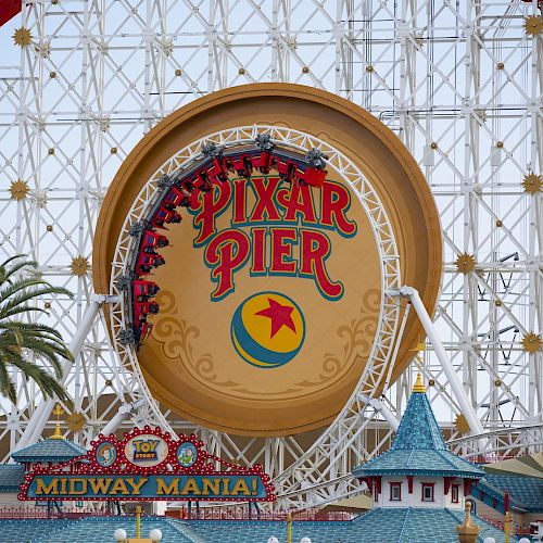 This image shows Pixar Pier with its iconic Ferris wheel and sign, located at a theme park. The Midway Mania attraction can also be seen.