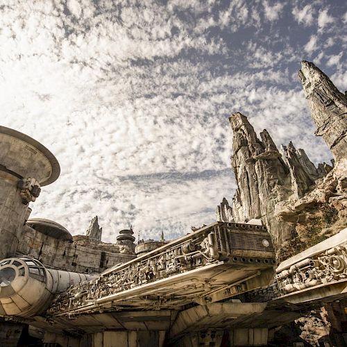 A large, detailed spacecraft is set against a rugged, rocky landscape with a sky filled with dramatic clouds, resembling a sci-fi scene.