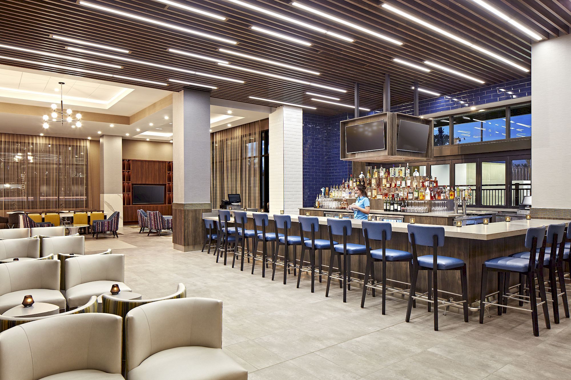 This image features a modern bar area with a long counter, multiple bar stools, and a well-stocked bar, with comfortable seating and stylish lighting.