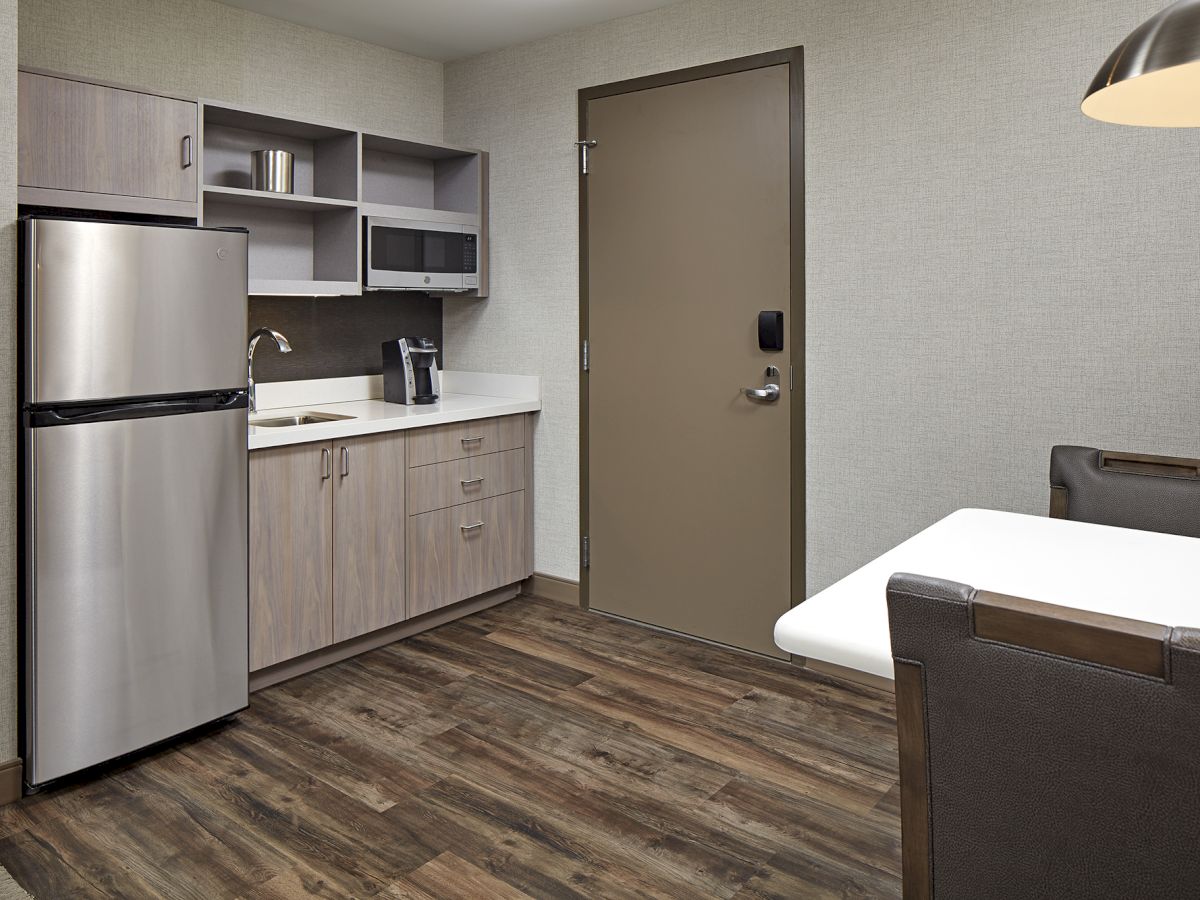 A small kitchen area with a refrigerator, microwave, sink, and cabinets, next to a table with chairs and a door.