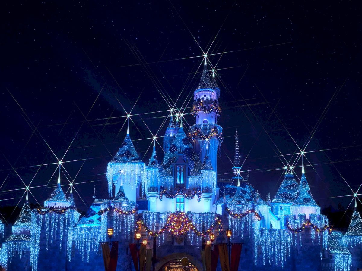 The image shows a castle illuminated with bright blue lights, covered in icy decorations, under a starry night sky.