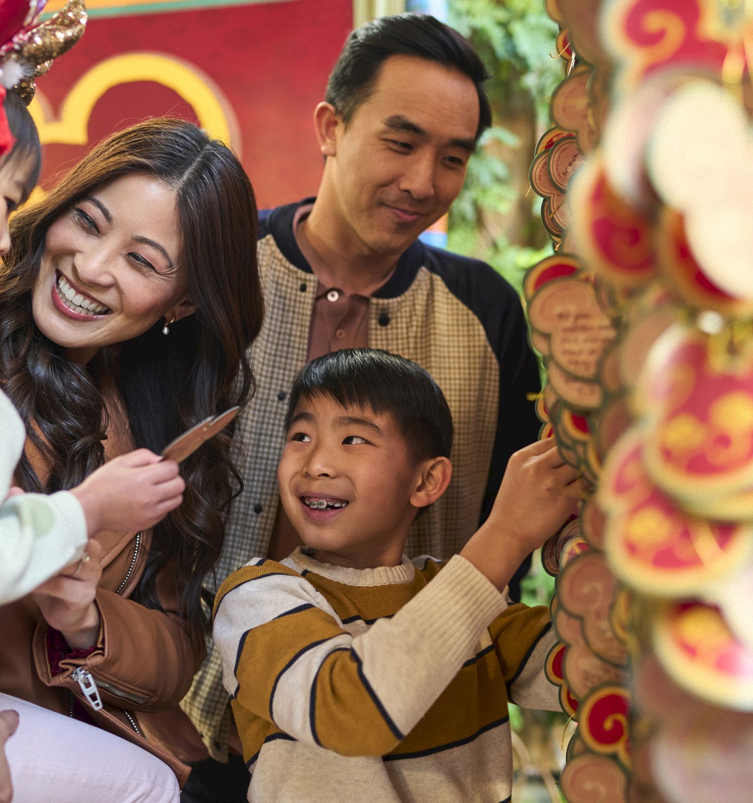 A family of four is smiling and enjoying an activity with decorative hanging ornaments in a festive setting.