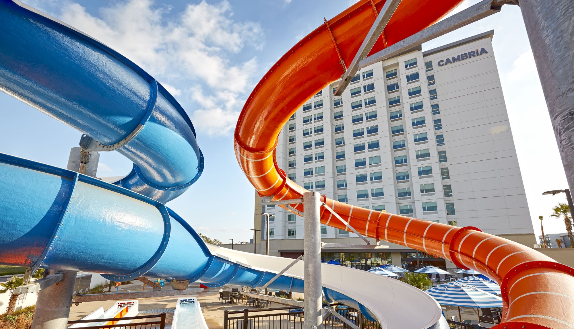 The image shows a hotel building with multiple colorful water slides, including blue, orange, and white slides, set against a sunny sky.